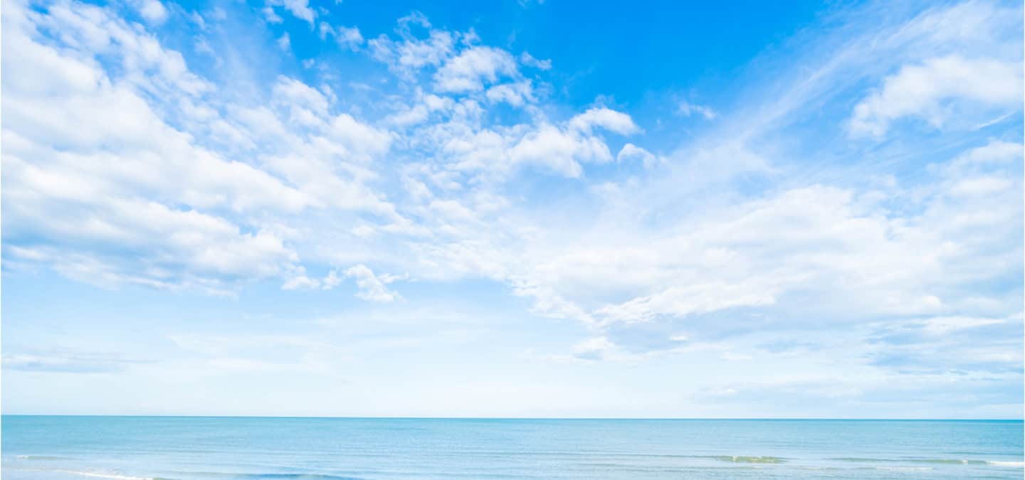 Blue sky with scattered clouds over calm turquoise sea at the horizon.